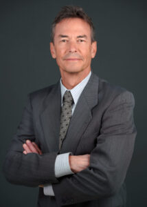 Professional portrait of Dr. Barry E. Gustin, toxicology expert witness, wearing a suit with arms crossed, conveying confidence and expertise in medical and forensic toxicology.