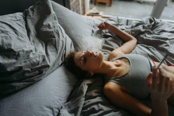 Young adult lying on a bed exhaling smoke, illustrating cannabis use related to anxiety and sleep issues.
